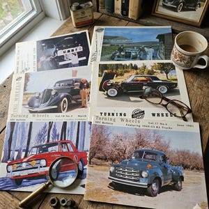 Könnte beinhalten: Eine Sammlung von Turning Wheels SDC Bulletin Magazinen mit Oldtimer-Autos und Lastwagen von Studebaker auf den Titelseiten, zusammen mit einer Lupe, Metallschrauben, einer Keramiktasse und einer kleinen Dose Uhrmacheröl.