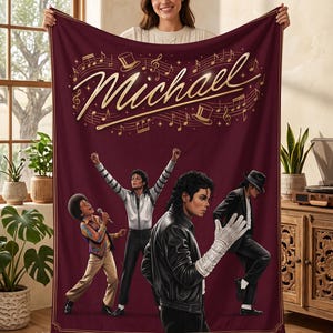 May include: A deep maroon fleece blanket featuring the name Michael in gold script at the top, surrounded by musical notes and top hats. Below, four illustrations depict a performer in various iconic outfits, including a leather jacket and glove.
