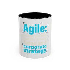 May include: A white ceramic mug with a black interior and rim. The exterior features the text 'Agile: because 'just think about it for a second' failed as a corporate strategy' printed in bright blue and light tan, accented by thin blue graphic lines.