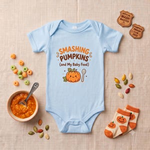 May include: A light blue baby bodysuit featuring the text SMASHING PUMPKINS (and My Baby Food) in orange and brown, with a cartoon pumpkin and spoon graphic. The design is centered on the chest of the short-sleeved garment with a snap closure.