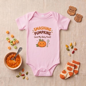 May include: A light pink baby bodysuit featuring the text SMASHING PUMPKINS (and My Baby Food) in orange and brown, with a cartoon pumpkin and a spoon graphic. The design is centered on the chest of the short-sleeved garment with a round neckline.
