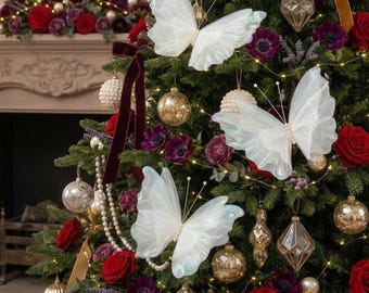 Könnte beinhalten: Drei große, irisierend weiße Schmetterlingsornamente mit zarten, durchscheinenden Flügeln und perlenartigen Zentren sind an einem Weihnachtsbaum befestigt, der mit goldenen Kugeln, Perlenketten sowie dunkelroten und violetten Rosen geschmückt ist.