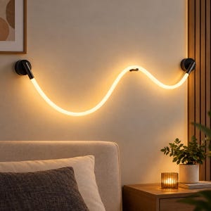 Pode incluir: Uma luminária de parede LED com um tubo flexível, ondulado e iluminado que emite um brilho amarelo quente. A luz é fixada em ambas as extremidades por dois suportes circulares de metal preto e inclui um pequeno suporte de fixação central.