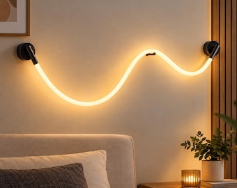Könnte beinhalten: Eine wandmontierte LED-Leuchte mit einem flexiblen, wellenförmigen, beleuchteten Schlauch, der ein warmes gelbes Licht ausstrahlt. Die Leuchte ist an beiden Enden mit runden schwarzen Metallhalterungen befestigt und hat eine kleine Stütze.