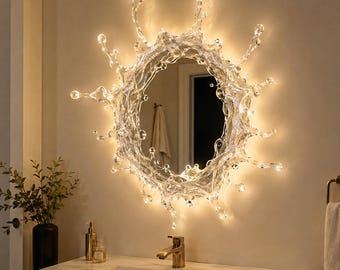 Könnte beinhalten: Ein runder Wandspiegel mit einem klaren, transparenten Rahmen, der wie ein Flüssigkeitsspritzer geformt ist. Der Rahmen wird durch integrierte warme LED-Lichter beleuchtet, die den unregelmäßigen, spitzen Kanten des Spritzer-Designs folgen.