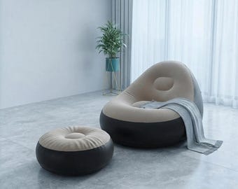 Könnte beinhalten: Ein aufblasbarer Loungesessel mit passendem runden Hocker in zweifarbigem Design mit beiger Oberseite und dunkelgrauer Basis. Eine hellgraue, strukturierte Decke liegt über der Sitzfläche des Sessels, der eine abgerundete Rückenlehne hat.