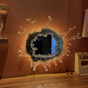 Close-up of the sculptural water splash design surrounding the acrylic mirror, showing the flowing irregular shape and illuminated LED edge.