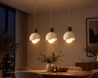 Könnte beinhalten: Eine lineare Pendelleuchte mit drei Hängelampen, die an einer rechteckigen Deckenplatte befestigt sind. Jede Lampe besteht aus einem dunkelgrünen, kugelförmigen Akzentteil über einem weißen, kuppelförmigen Schirm mit einer leuchtenden Kugel.