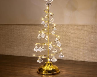 Könnte beinhalten: Eine spiralförmige Weihnachtsbaumdekoration aus goldfarbenem Metall mit einem Mittelstab, einem Stern als Spitze und integrierten LED-Lichtern. Klare, diamantförmige Anhänger hängen am spiralförmigen Drahtgestell, das auf einem runden Goldfuß steht.