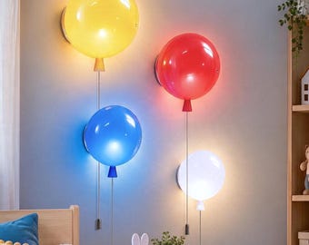 Könnte beinhalten: Vier wandmontierte ballonförmige Lampen in Gelb, Rot, Blau und Weiß. Jede Lampe hat einen kugelförmigen Schirm, einen kleinen Sockel und eine dünne Zugschnur, die mit einem kleinen Gewicht nach unten hängt und ein sanftes Licht abgibt.