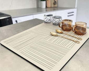Könnte beinhalten: Eine rechteckige, cremefarbene Tischmatte mit einem Muster aus dünnen, dunkelgrauen horizontalen und vertikalen Linien. Zwei klare, strukturierte Gläser, zwei bernsteinfarbene Gläser und zwei goldfarbene Metalllöffel liegen darauf.