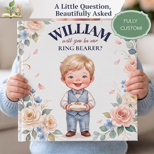 Peut inclure: Une couverture de livre carrée avec le texte A Little Question, Beautifully Asked, William, et will you be our RING BEARER? Elle présente une illustration de dessin animé d'un jeune enfant en costume bleu tenant un coussin d'alliances avec deux anneaux dorés, entouré de roses roses et blanches et de fleurs bleues style aquarelle.