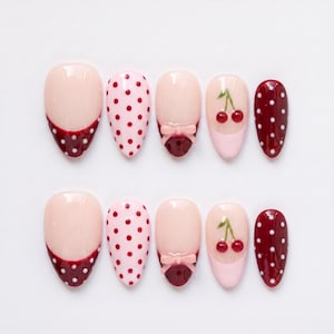May include: A set of ten almond-shaped press-on nails featuring a variety of designs including deep red French tips with white polka dots, light pink nails with red polka dots, solid light pink with a 3D bow, and light pink with cherry art.