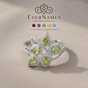 May include: A sterling silver S925 ring featuring five pear-shaped green peridot gemstones arranged in a floral pattern, accented with small clear stones. The text EverNames and 5 Natural Gemstones is visible above the ring with color icons.