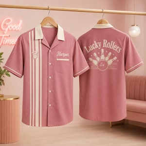 May include: A dusty rose short-sleeve button-down shirt with a cream-colored collar and vertical stripes on the front. The front features a small bowling pin graphic and the name Harper. The back displays the text Lucky Rollers with a bowling graphic.