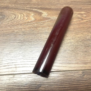 Könnte beinhalten: Ein zylindrisches, tiefburgunderfarbenes Objekt mit einer glatten, glänzenden Oberfläche. Der Gegenstand verfügt über ein abgerundetes oberes Ende und eine flache, kreisförmige Basis, was ein solides, einheitliches Erscheinungsbild ergibt.