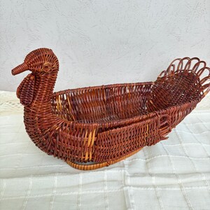 May include: A brown woven wicker basket shaped like a turkey. The basket features a detailed head with a beak and wattle, a hollow oval body for storage, and a fanned tail section made of looped wicker strands, all constructed from natural reed.