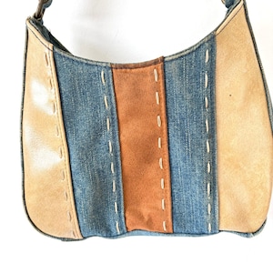 May include: A shoulder bag constructed from alternating vertical panels of blue denim, tan leather, and a central strip of rust-colored suede. The panels are joined by visible, thick cream-colored decorative stitching throughout the exterior surface.