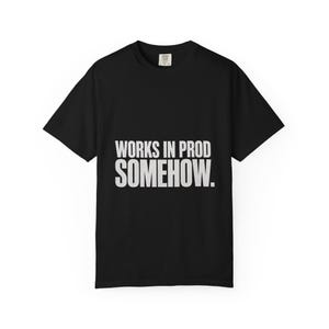 May include: A black short-sleeved t-shirt featuring the white text "WORKS IN PROD SOMEHOW." printed in a bold, sans-serif font across the centre of the chest. The garment has a crew neckline and a standard fit, with a small brand label at the neck.