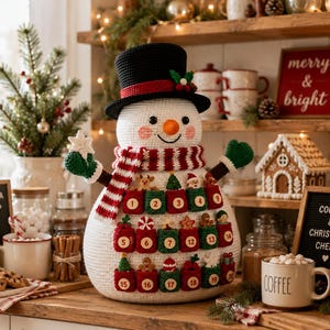 May include: A crocheted snowman advent calendar featuring a black top hat, a red and white striped scarf, and green mittens. The snowman body has twenty small red and green pockets numbered one through twenty, each decorated with tiny holiday ornaments.