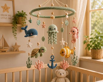 May include: A hanging nursery mobile featuring crocheted sea creatures including a blue whale, a green jellyfish, a pink seahorse, a green turtle, and a yellow fish, along with a blue anchor, coral shapes, and stars suspended from a green ring.