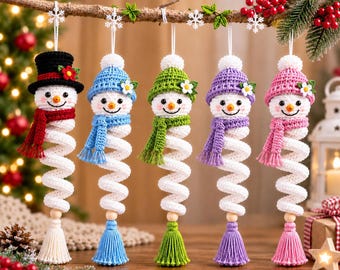 May include: Five crocheted snowman ornaments hanging in a row. Each snowman has a white spiral body, a wooden bead, and a colored tassel. They wear matching hats and scarves in black, blue, green, purple, and pink, each accented with a small flower.