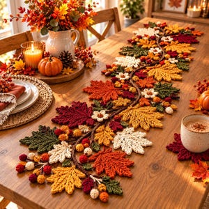 May include: A long, decorative table runner featuring a crocheted garland of autumn leaves in shades of red, orange, yellow, green, and cream, accented with small crocheted flowers, berries, and acorns, laid out on a wooden dining table.