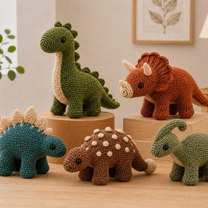 Op de afbeelding: Een verzameling van vijf gehaakte dinosaurus-speeltjes in verschillende kleuren en soorten. De set bevat een lange groene dinosaurus met een lange nek, een roestkleurige triceratops, een blauwgroene stegosaurus met beige platen, een bruine ankylosaurus en een lichtgroene parasaurolophus.