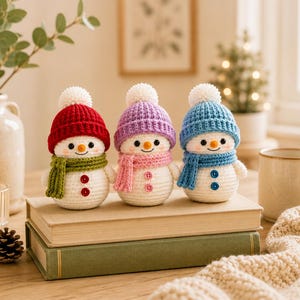 Peut inclure: Trois petites figurines de bonhommes de neige au crochet avec des corps blancs, des nez orange et des yeux noirs. Chacun porte un bonnet en tricot de couleur diff&eacute;rente avec un pompon blanc et une &eacute;charpe assortie. Le bonhomme de neige de gauche a un bonnet rouge et une &eacute;charpe verte, celui du milieu un bonnet violet et une &eacute;charpe rose, et celui de droite un bonnet et une &eacute;charpe bleus. Chacun a deux petits boutons sur le devant.