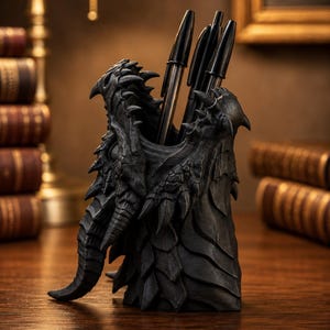 Peut inclure: Un organisateur de bureau noir et texturé en forme de tête de dragon avec des écailles et des cornes. Le récipient cylindrique contient trois stylos à bille noirs. La surface présente des détails complexes en relief imitant la peau.