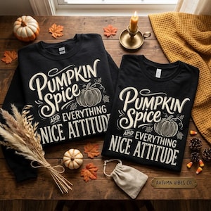 Pode incluir: Duas camisas pretas de manga comprida com o texto branco Pumpkin Spice and Everything Nice Attitude e uma ilustração de abóbora. As camisas estão dispostas com pequenas abóboras, talos de trigo secos, uma vela e uma pequena bolsa de tecido.