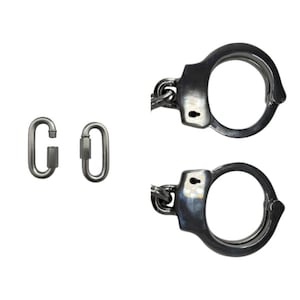 Könnte beinhalten: Ein Paar dunkelmetallische Handschellen mit glatter Oberfläche und zwei ovale Schraubkarabiner. Die Handschellen haben ein kreisförmiges Design mit einem Schlüssellochmechanismus, während die Karabiner einen Schraubverschluss besitzen.