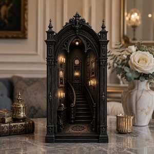 Könnte beinhalten: Ein schwarzes, detailliertes Miniatur-Diorama eines gotischen Interieurs mit einer großen Treppe, Wandporträts und beleuchteten Wandleuchtern. Die Struktur hat einen Bogengiebel, kunstvolle architektonische Schnitzereien und eine zentrale Uhr.