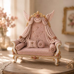 May include: A miniature sofa in dusty pink with gold trim, featuring a tufted backrest, draped fabric accents, and decorative angel wings at the top. The piece includes a square and a round throw pillow, all finished with intricate floral details.