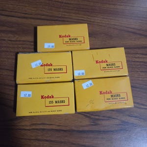 May include: Five rectangular yellow Kodak boxes for glass slide masks. Three boxes are labeled Kodak Masks for Glass Slides 2 x 2 in. (5.1 x 5.1 cm) and two boxes are labeled Kodak 135 Masks for 2 x 2 in. (5.1 x 5.1 cm) glass slides.