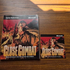 May include: A large rectangular game reference manual and a smaller square booklet for the video game Close Combat by Microsoft. Both feature a soldier in a helmet using a field telephone with the title Close Combat and the text Take command of men who act like real soldiers.