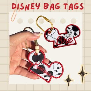 Peut inclure: Deux étiquettes de sac en tissu en forme de Mickey Mouse avec des bordures cousues rouges. Une étiquette porte le nom Bre brodé en rouge, et l'autre le nom Karissa brodé en rouge. Les deux incluent des anneaux métalliques dorés et des perles.