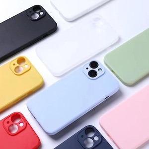 Peut inclure: Une collection de coques de smartphone unies dans diverses teintes, notamment noir, blanc, jaune, bleu clair, vert clair, rose, rouge et bleu foncé. Chaque coque présente une découpe carrée pour l'appareil photo avec des ouvertures circulaires.