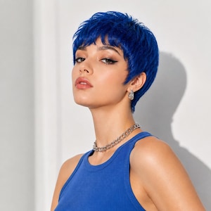 Puede incluir: Una peluca corta y degradada de color azul vibrante con un acabado texturizado en mechones y flequillo suave. El cabello está peinado en un corte estilo pixie que enmarca el rostro, con un color azul cobalto profundo y saturado en todo el pelo.
