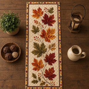 May include: A rectangular quilted table runner featuring a central design of autumn maple leaves in shades of red, orange, yellow, and green, accented with small berries. The runner has a cream-colored background and a border with leaf motifs.