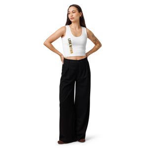 May include: A white sleeveless crop top featuring the text LOOK WITHIN printed vertically in gold on the right side, paired with high-waisted black wide-leg trousers that have a pleated front and a full-length, loose-fitting silhouette.