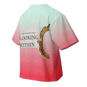 May include: A short-sleeve t-shirt featuring a mint green to red gradient. The back displays a gold ornate mirror frame graphic and the text: The ultimate clarity is found LOOKING WITHIN. The design includes a white paper-like background element.