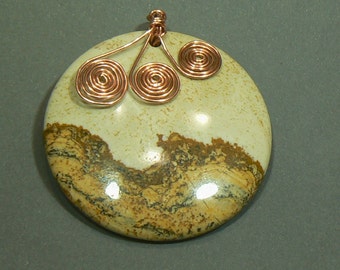May include: A circular pendant with a beige stone, displaying brown and black patterns. Copper wire is used to create three spiral designs at the top. This pendant is a unique piece of jewellery.