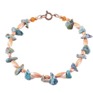 May include: A handcrafted necklace featuring turquoise-colored stone beads and copper-colored metal beads. The necklace has a copper-colored clasp and is displayed against a white background. The necklace is a piece of jewelry.