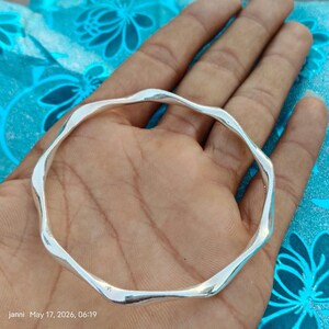 May include: A polished silver bangle bracelet featuring a continuous wavy, undulating edge design. The metal surface is smooth and reflective, forming a circular shape with a consistent thickness throughout the entire circumference of the jewellery piece.