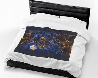 Puede incluir: Una funda nórdica blanca con una manta rectangular que muestra una escena de cielo nocturno en azul oscuro. El estampado presenta una luna llena brillante, ventanas doradas iluminadas y estructuras arquitectónicas sobre un fondo azul marino.