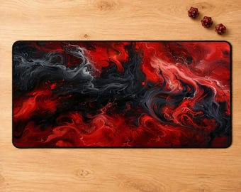 May include: A rectangular desk mat featuring a vibrant abstract design of swirling red, black, and white ink-like patterns. The surface displays fluid, smoke-like textures that blend across the mat. Three small red polyhedral dice are nearby.