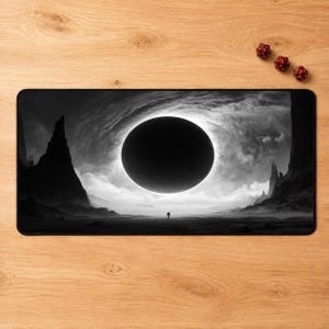 May include: A rectangular desk mat featuring a black and white landscape illustration of a large, dark circular eclipse centered in a cloudy sky above a barren terrain with sharp rock formations and a small silhouette figure in the distance.