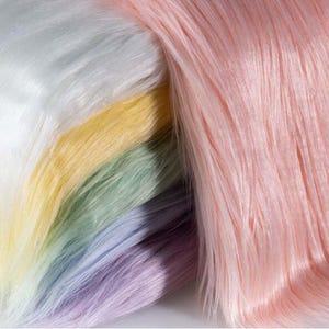May include: A collection of faux fur fabric swatches in a layered arrangement. The colors include white, pale yellow, soft mint green, light lavender, and a prominent section of pastel pink. Each piece features a long, straight, synthetic pile.