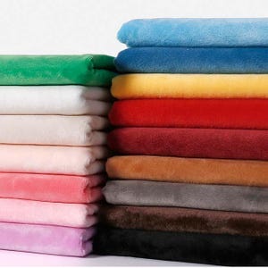 Può includere: Una pila di pezzi di tessuto piegati in una varietà di colori solidi tra cui azzurro, blu scuro, giallo, rosso, bordeaux, beige, grigio, marrone, nero, verde, bianco, crema, rosa chiaro e lavanda. Ogni pezzo ha una consistenza morbida e felpata.